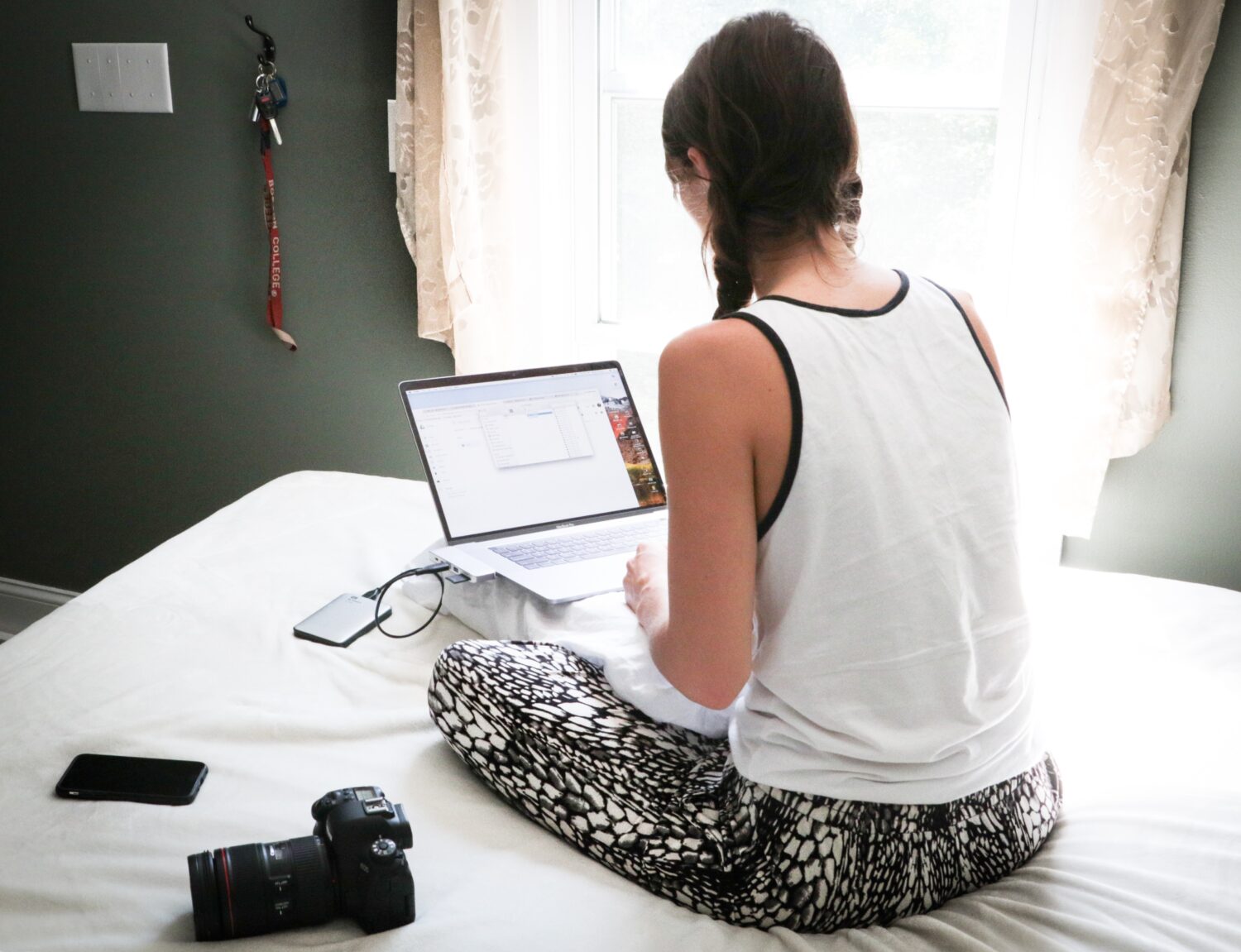 Woman in white tank top sitting on laptop on bed college planning